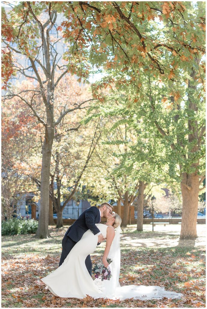 groom dips his bride way back as they kiss by colorful fall trees in philadelphia pennsylvania