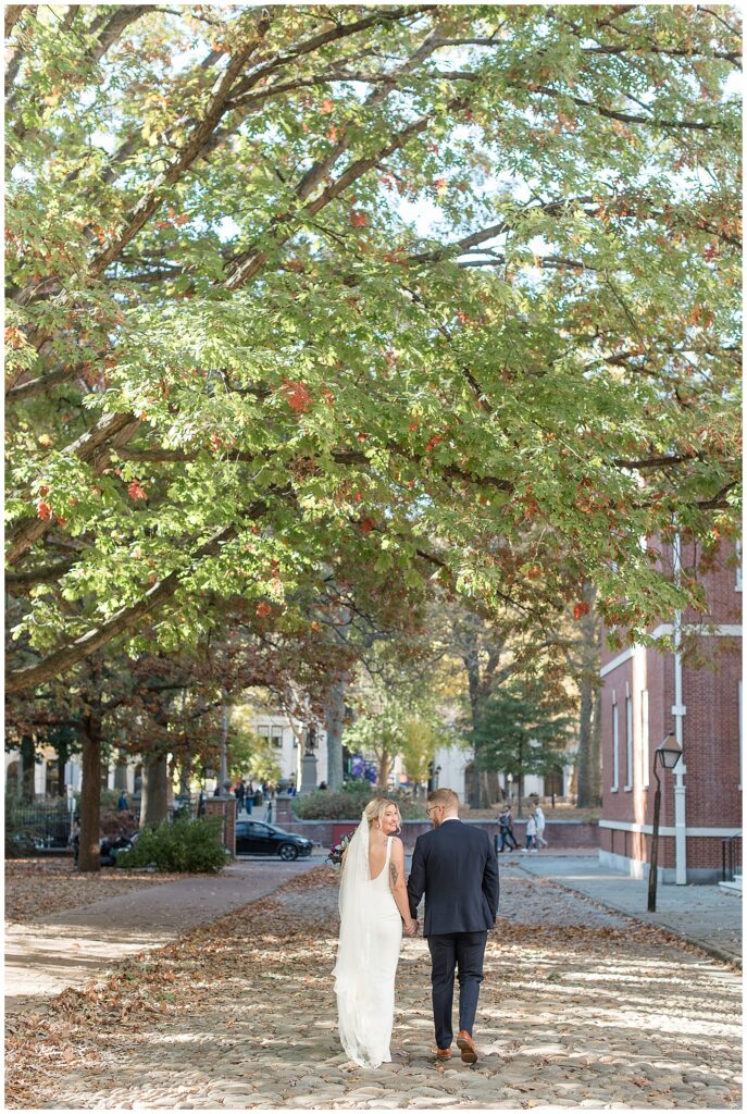 couple holding hands and walking down street away from camera on sunny fall day in philadelphia