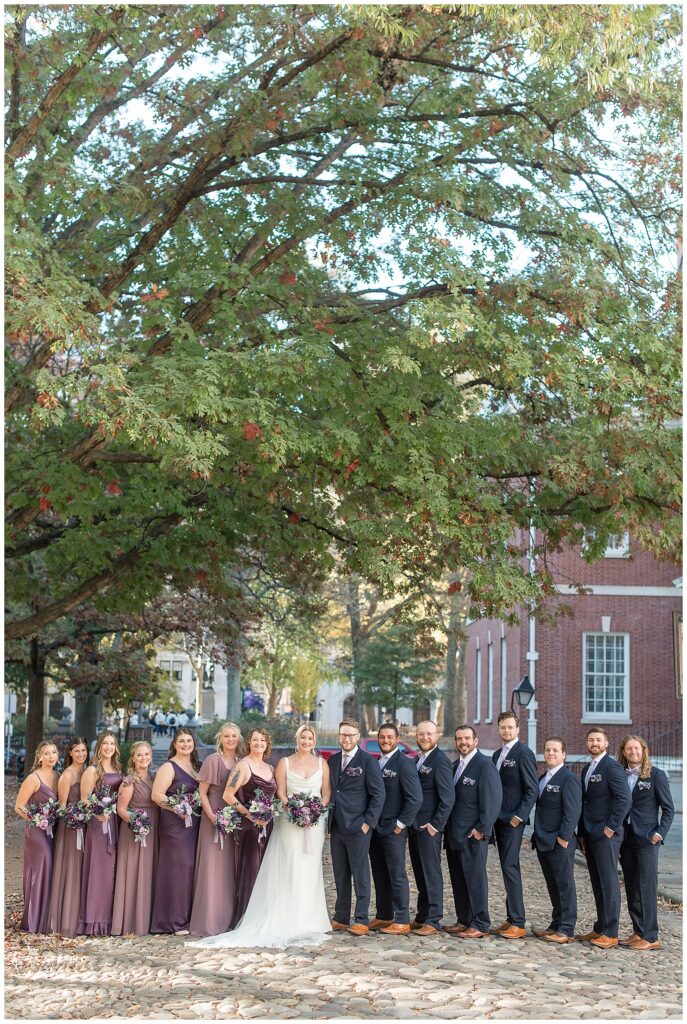 couple surrounded by their large bridal party  in downtown philadelphia by tree and city buildings