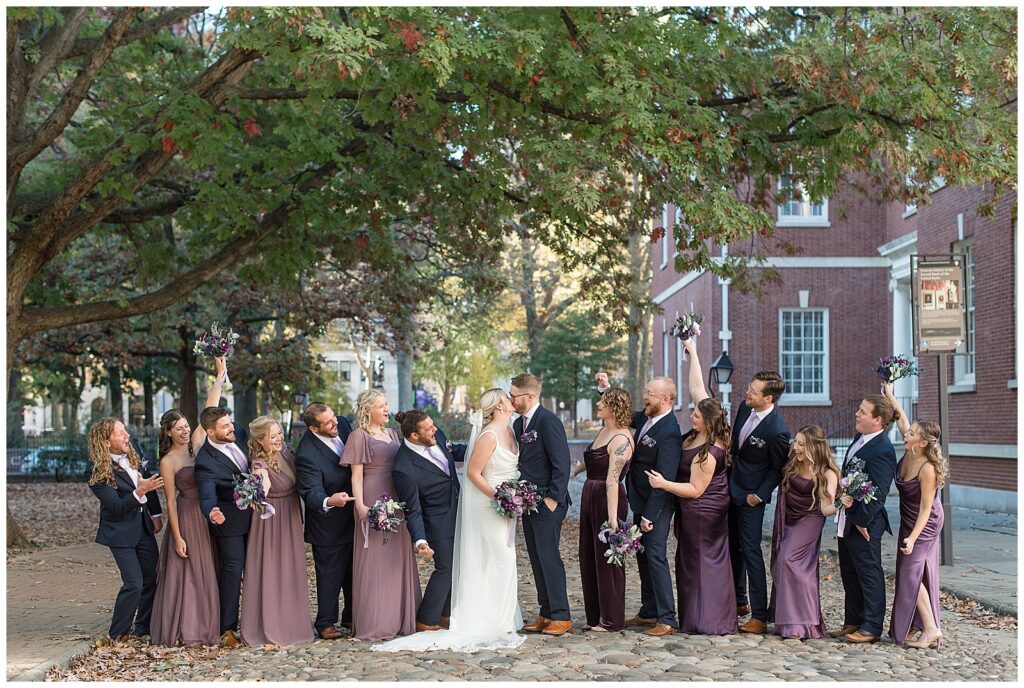 couple kissing as their bridal party surrounds them and cheers in downtown philadelphia