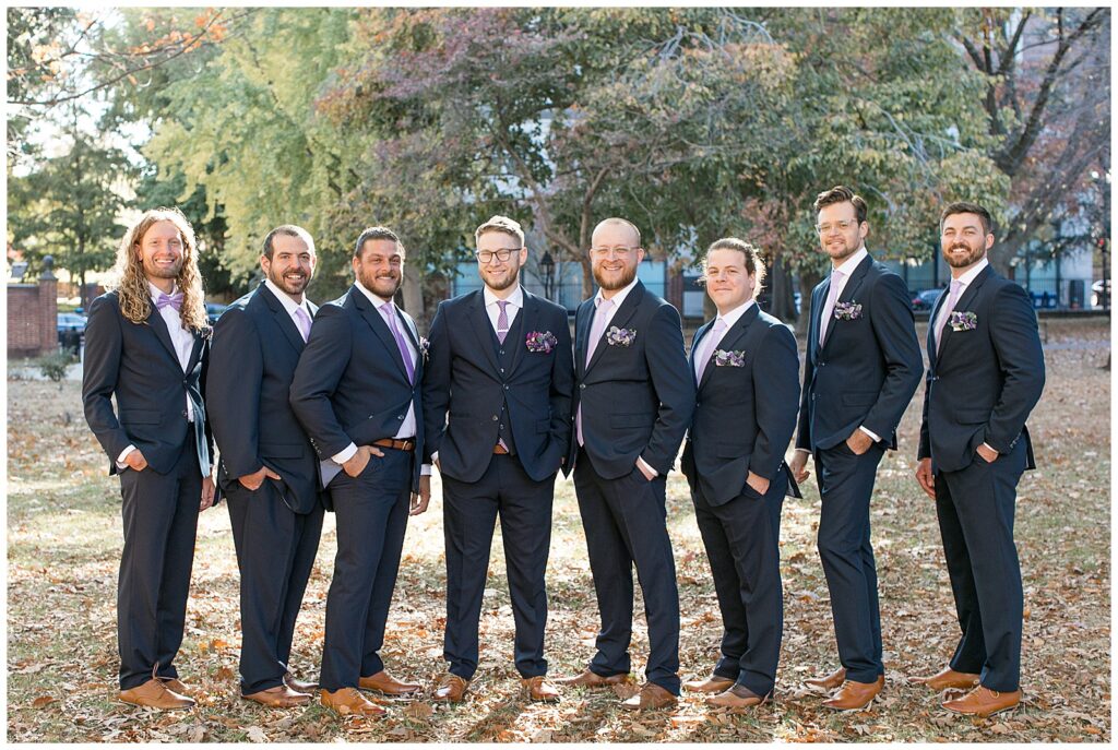 groom with his seven groomsmen all in dark suits with mauve ties and their hands in their pockets in philadelphia