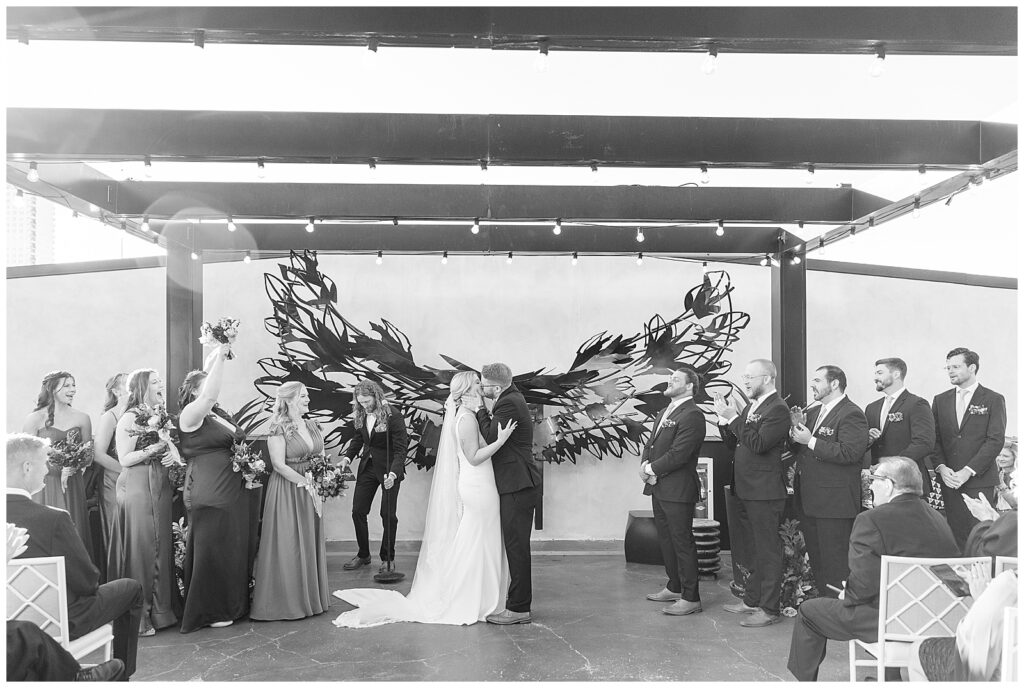 stunning black and white photo of couple sharing their first kiss during indoor wedding ceremony at kimpton hotel monaco philadelphia