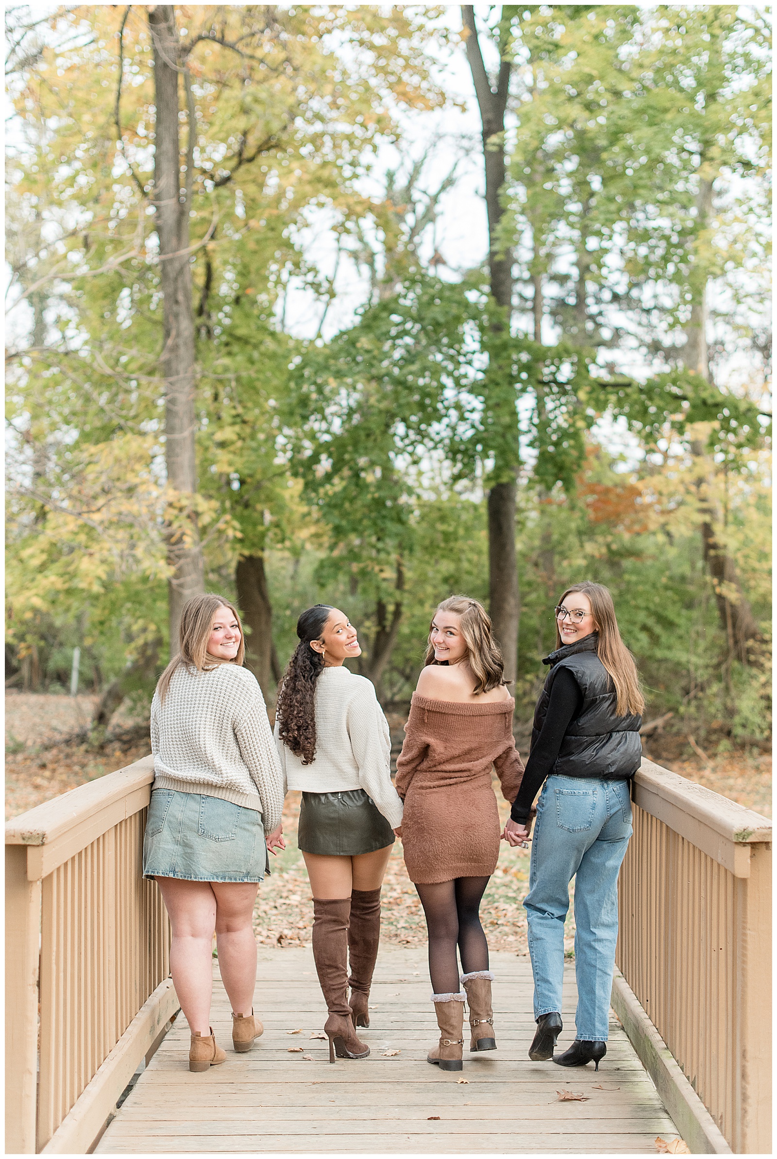 four senior girls on wooden bridge with backs toward camera as they look back and smile in lancaster county