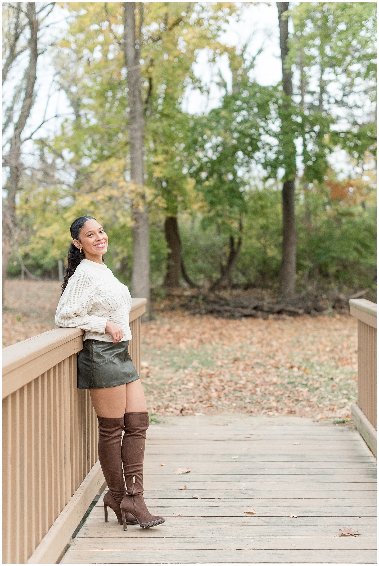 senior girl leaning back against wooden bridge with colorful fall trees behind her in lancaster pa