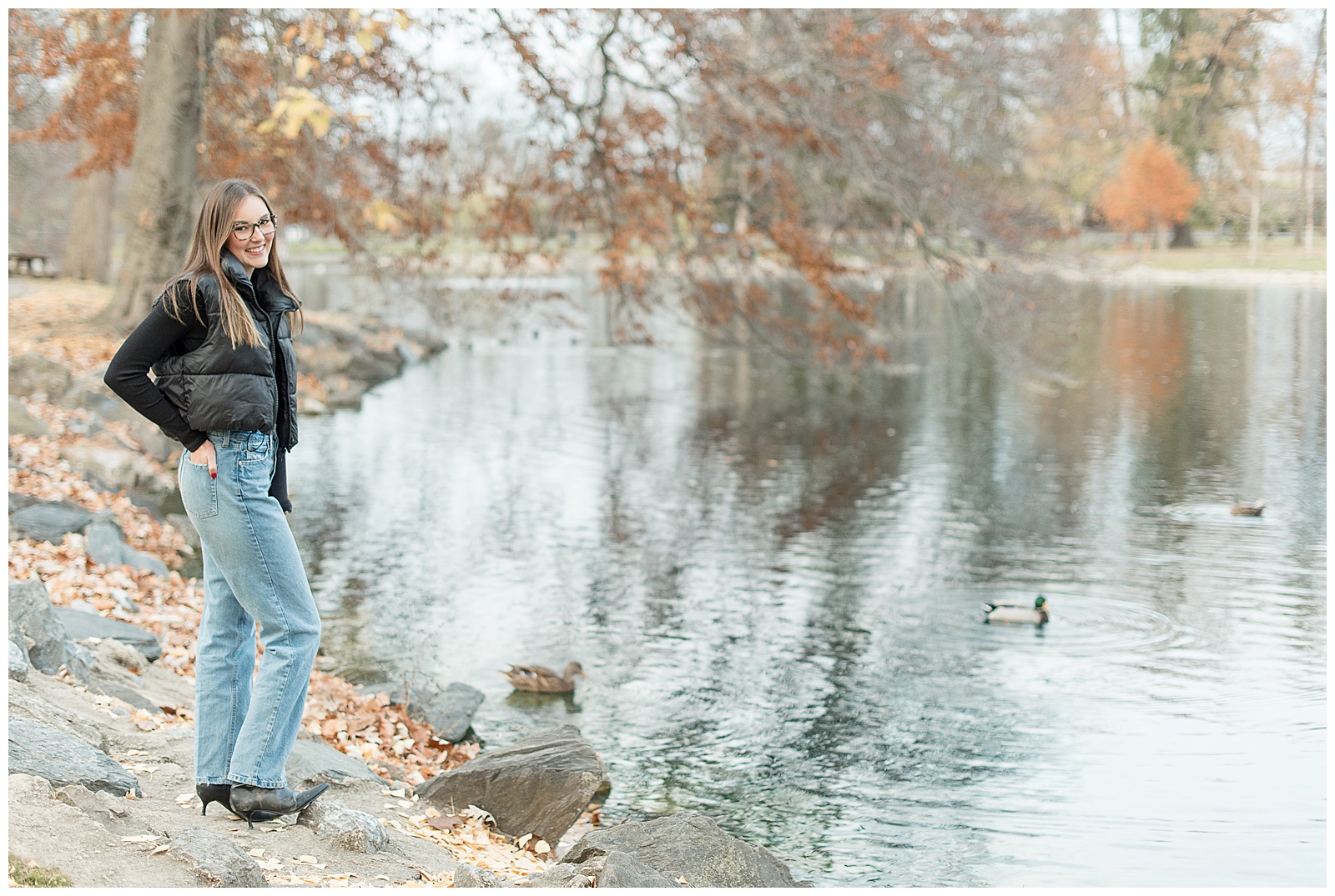 senior girl standing along edge of pond with right hand on hip at long's park on fall day