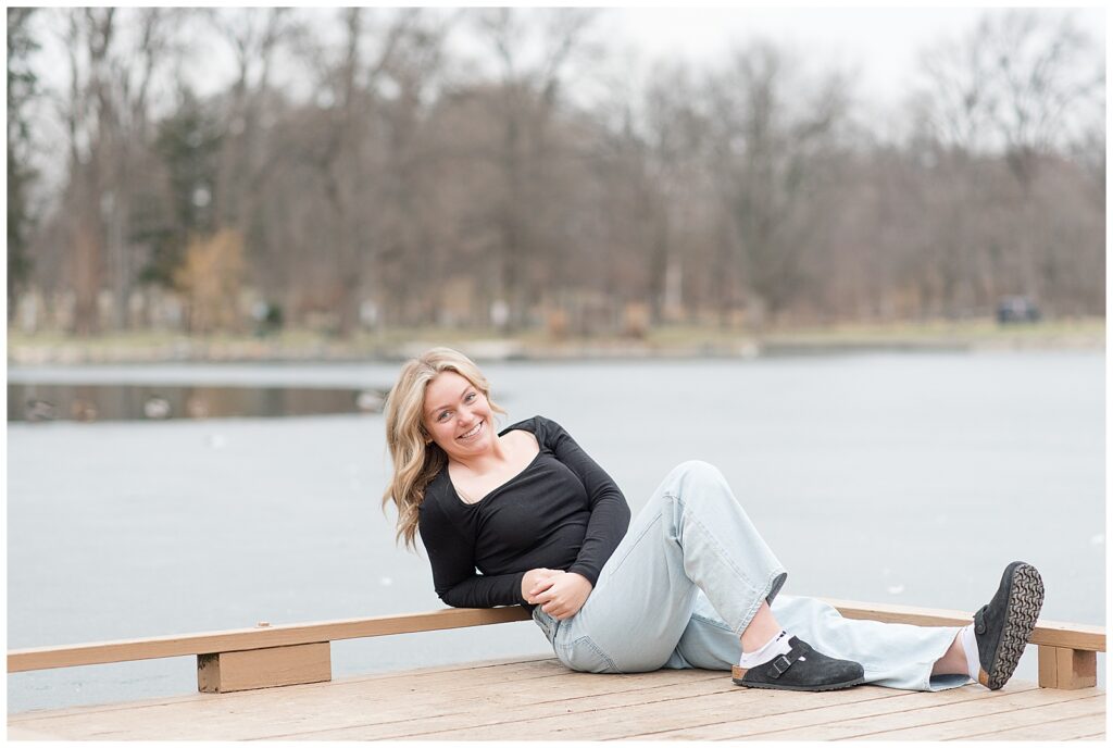 class of 2025 senior girl in black top with blue jeans sitting on dock at longs park in lancaster county