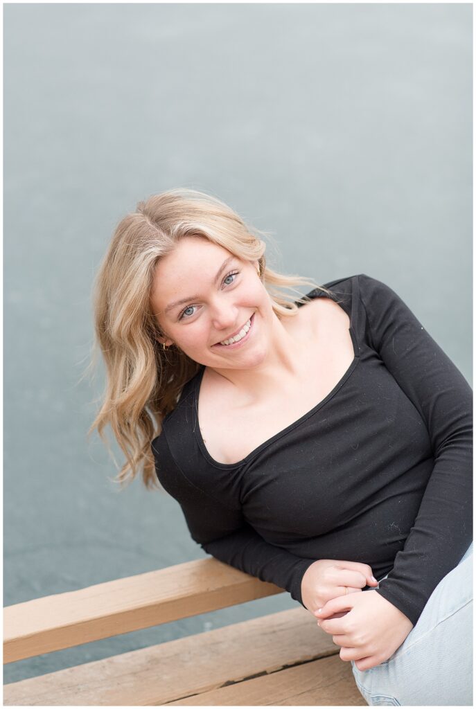 senior girl in black top leaning on right elbow of pond dock at longs park