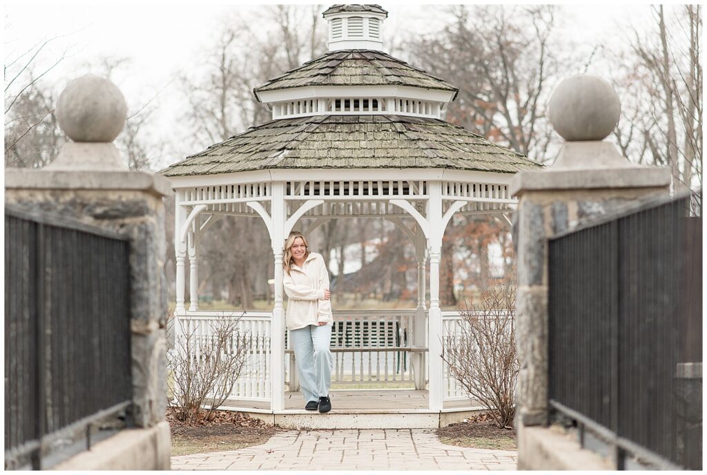 class of 2025 senior girl in ivory sweatshirt and blue jeans leaning against white gazebo column at longs park in lancaster pa