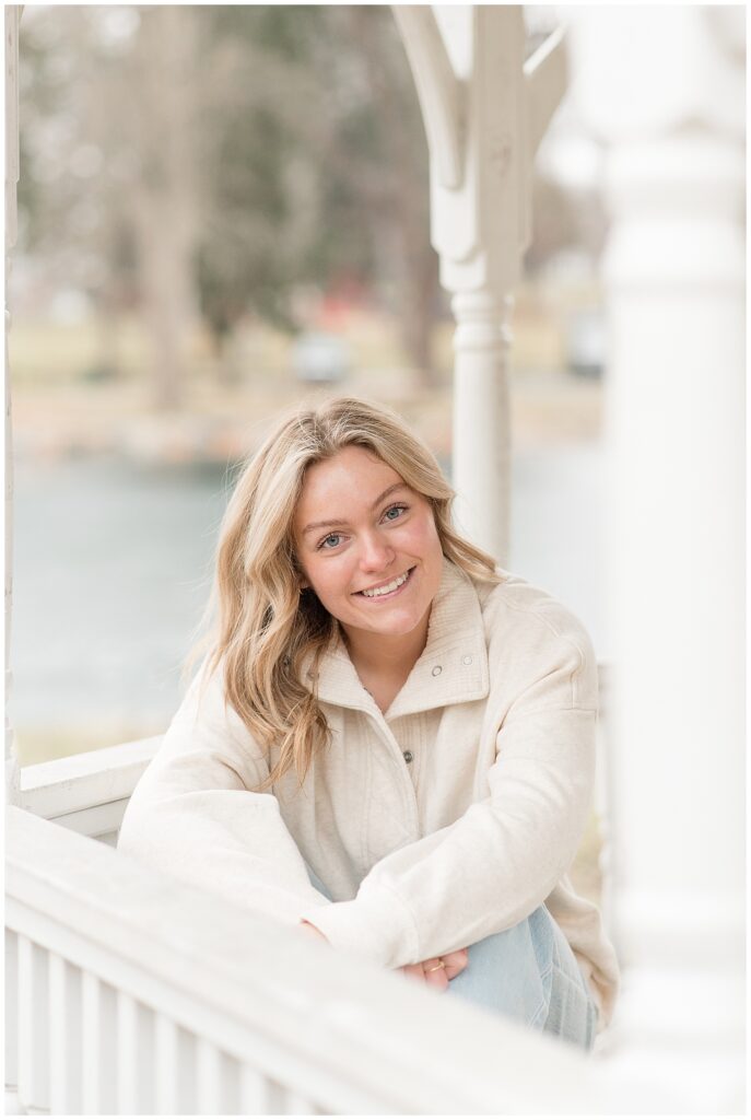 senior girl sitting on bench in gazebo by pond on winter day in lancaster pennsylvania