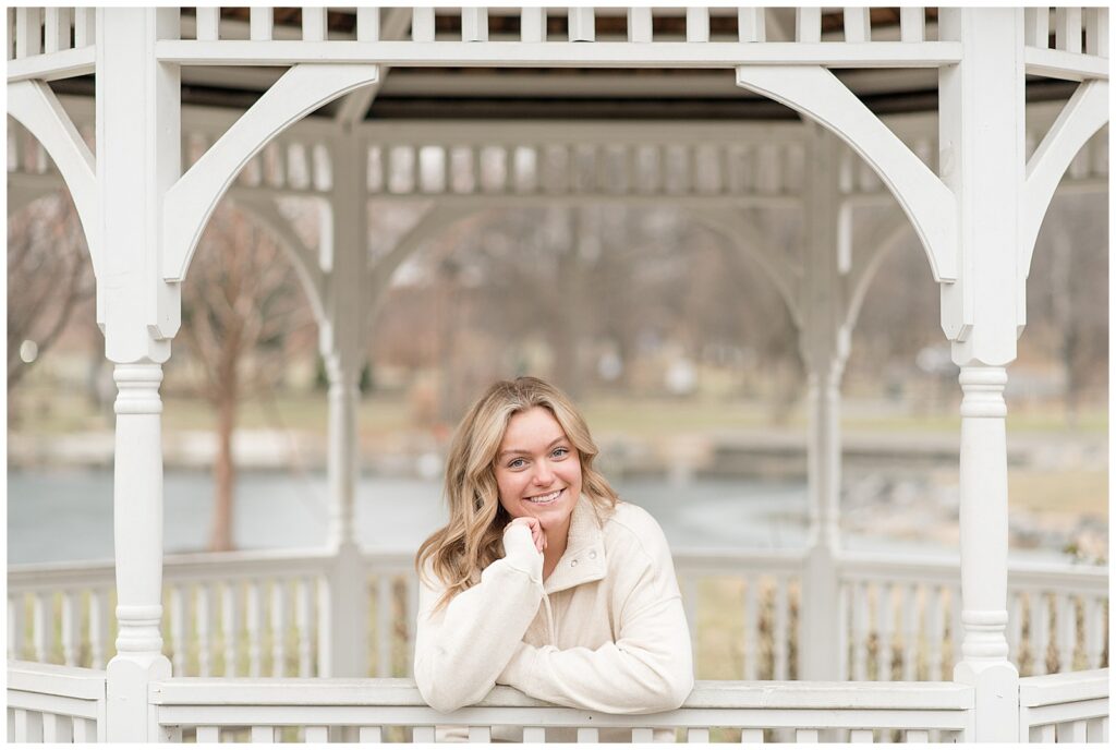 senior girl leaning on edge of gazebo with longs park pond behind her on sunny winter day