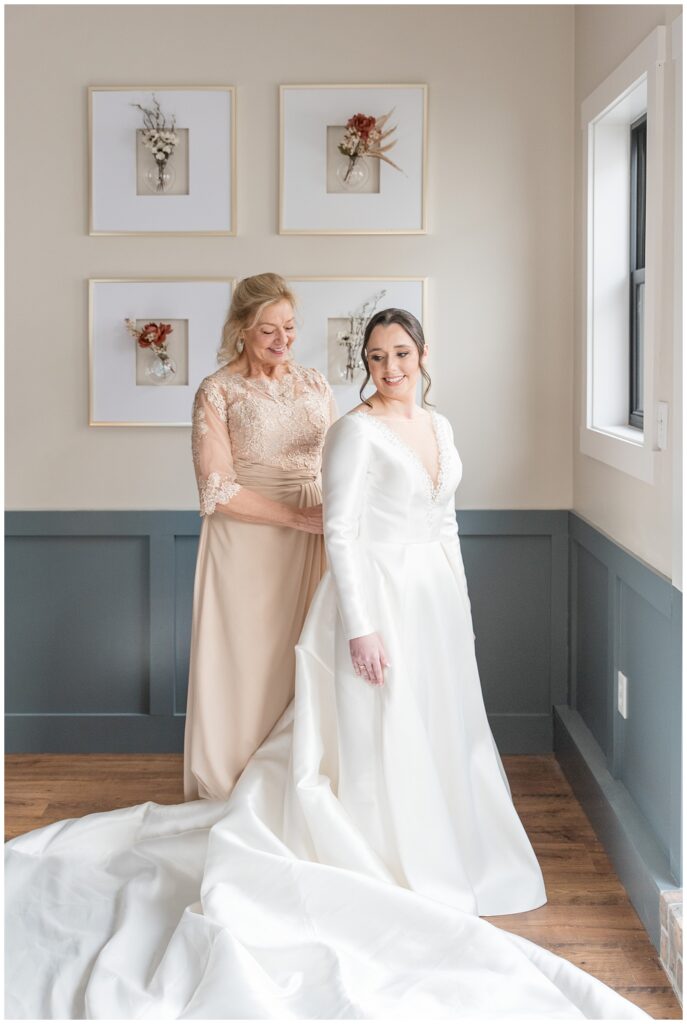 mother of the bride zipping up bride's white wedding gown in bridal suite at ironspire complex