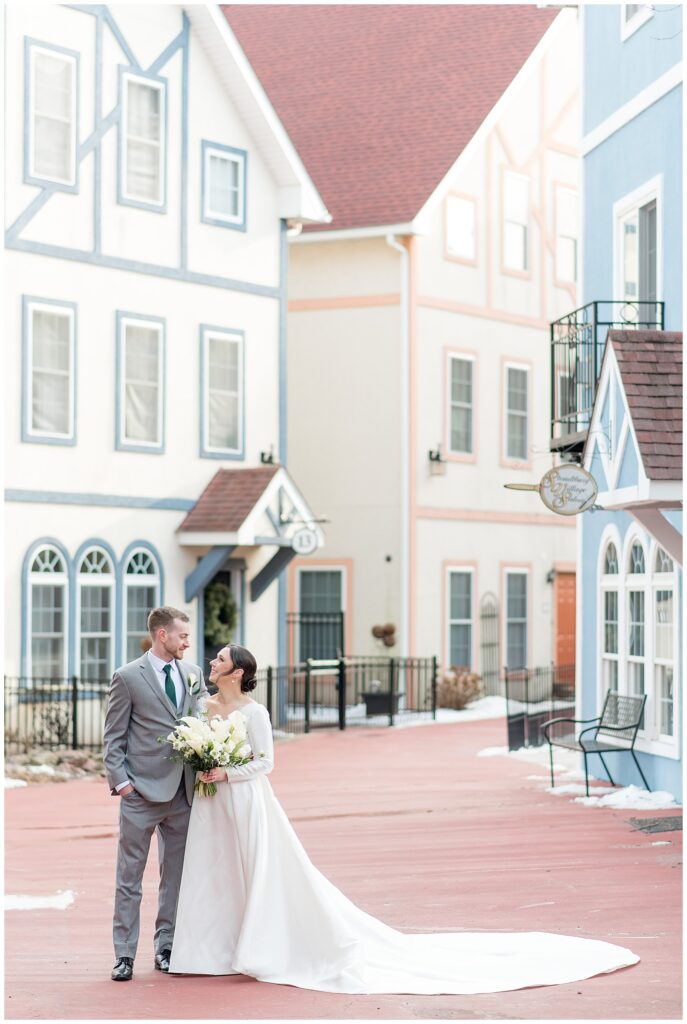 bride and groom smiling at each other with colorful buildings behind them at stoudtburg village in lancaster county