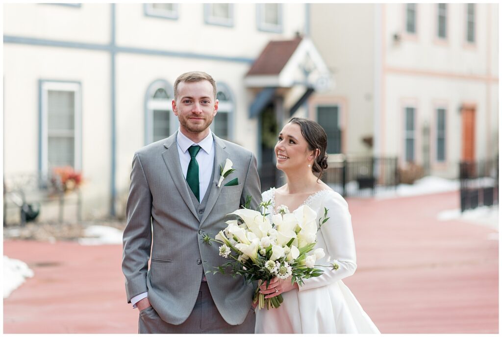 bride looking at her groom as they both smile at stoudtburg village on a cold winter day