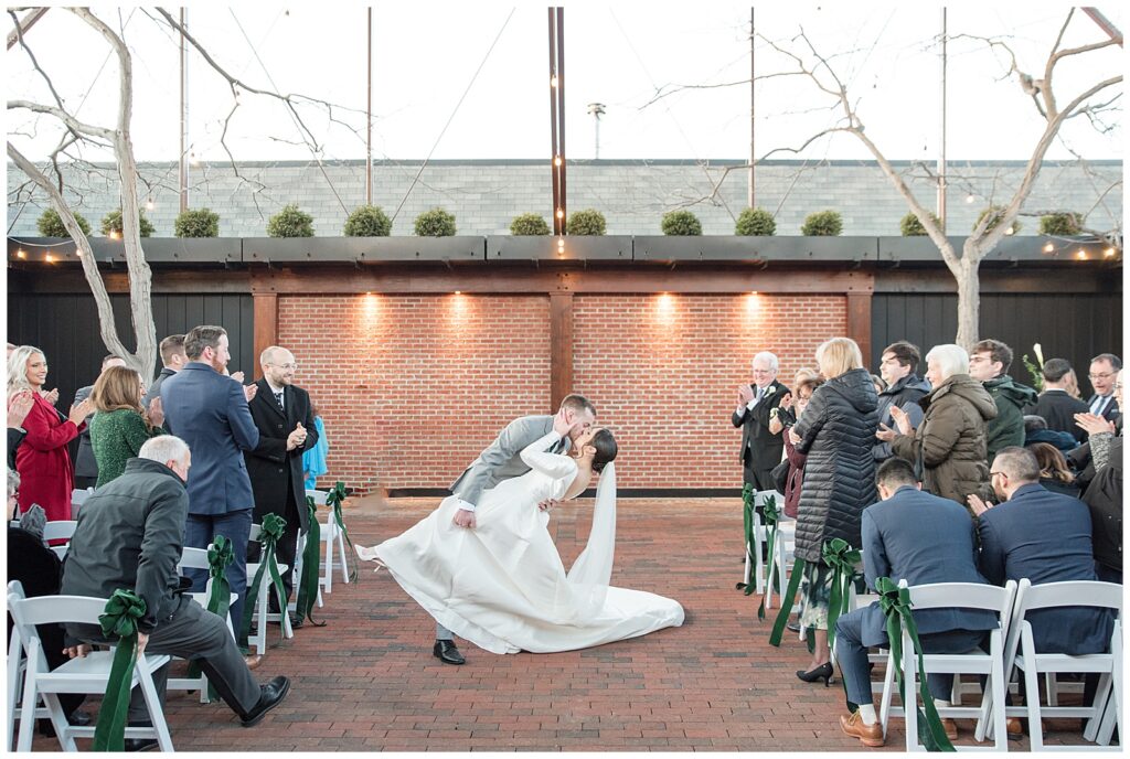 groom dipping back his bride as they kiss leaving outdoor winter wedding ceremony at ironspire complex