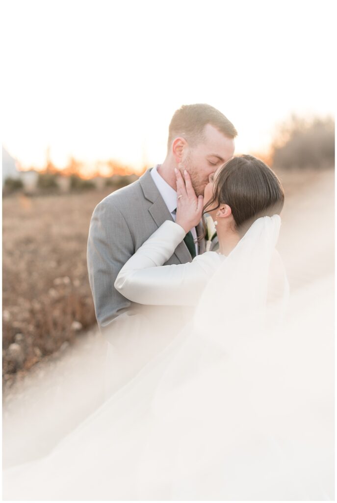 bride holding groom's jawline as they kiss in field at sunset in adamstown pennsylvania