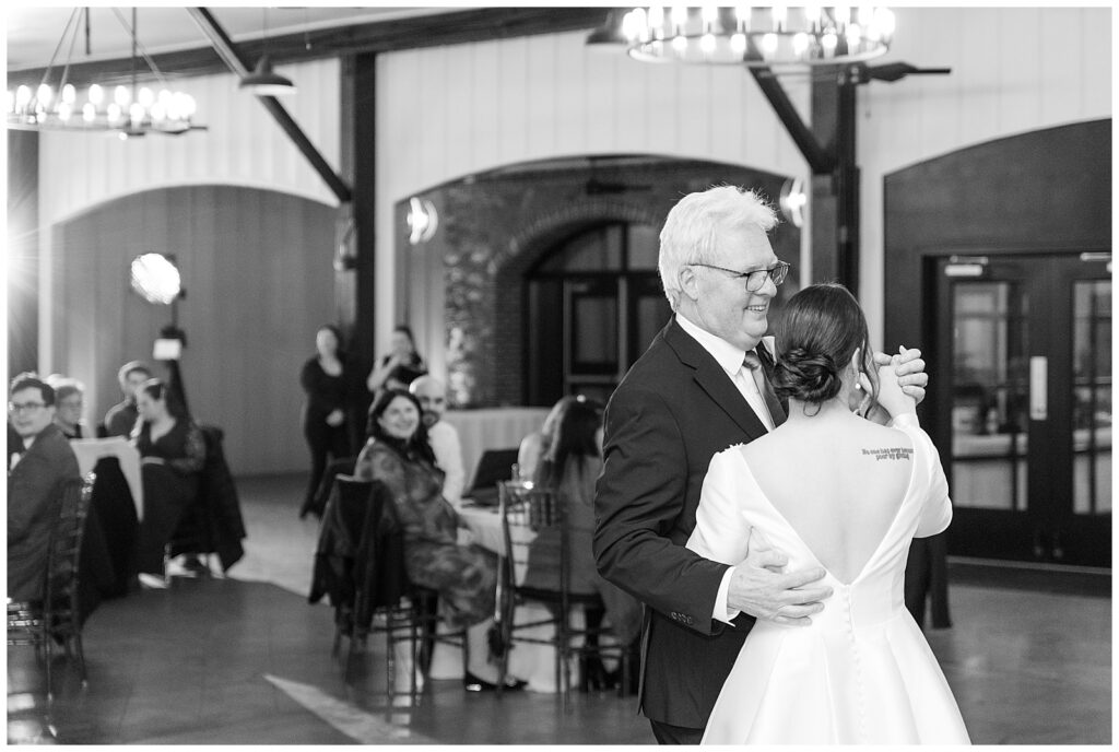 black and white photo of bride dancing with her father with her back toward the camera at ironspire complex in pennsylvania