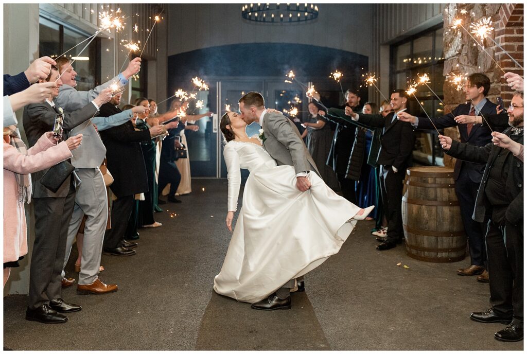 groom dipping back his bride and holding onto her right knee in middle of aisle as guests raise sparkler in lancaster pennsylvania