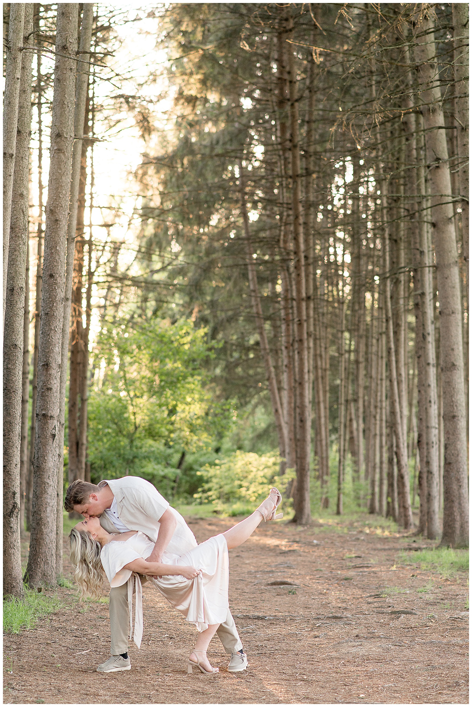 guy dips girl back as they kiss by evergreen tree grove at sunset at overlook park