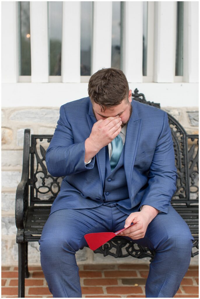 groom sitting on bench reading note from his soon-to-be wife and crying at the star barn