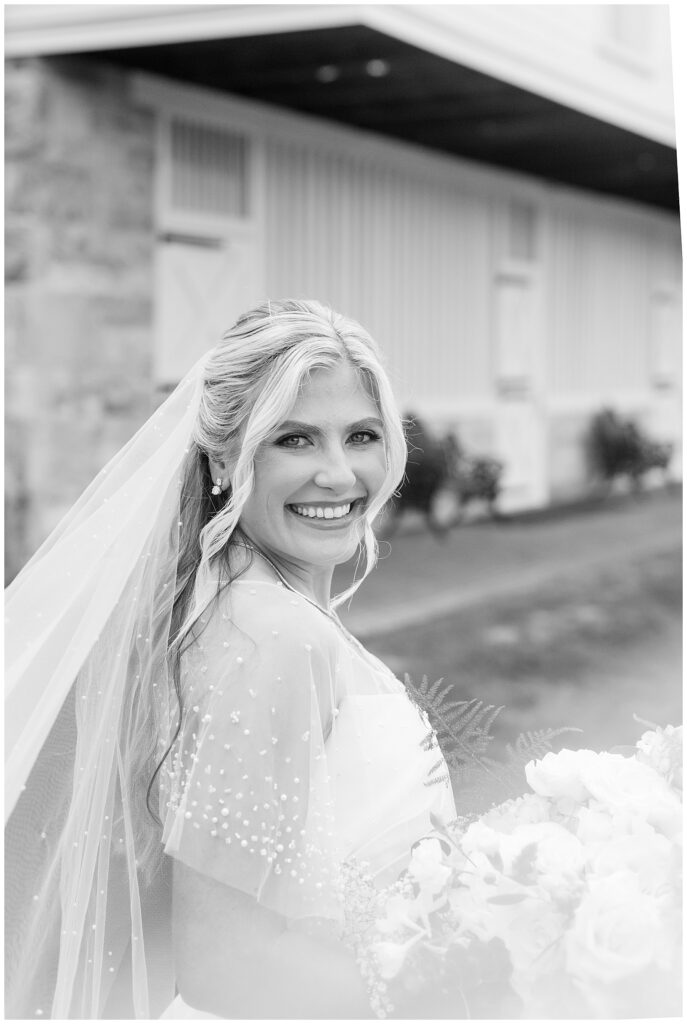 black and white photo of bride smiling at camera with star barn behind her