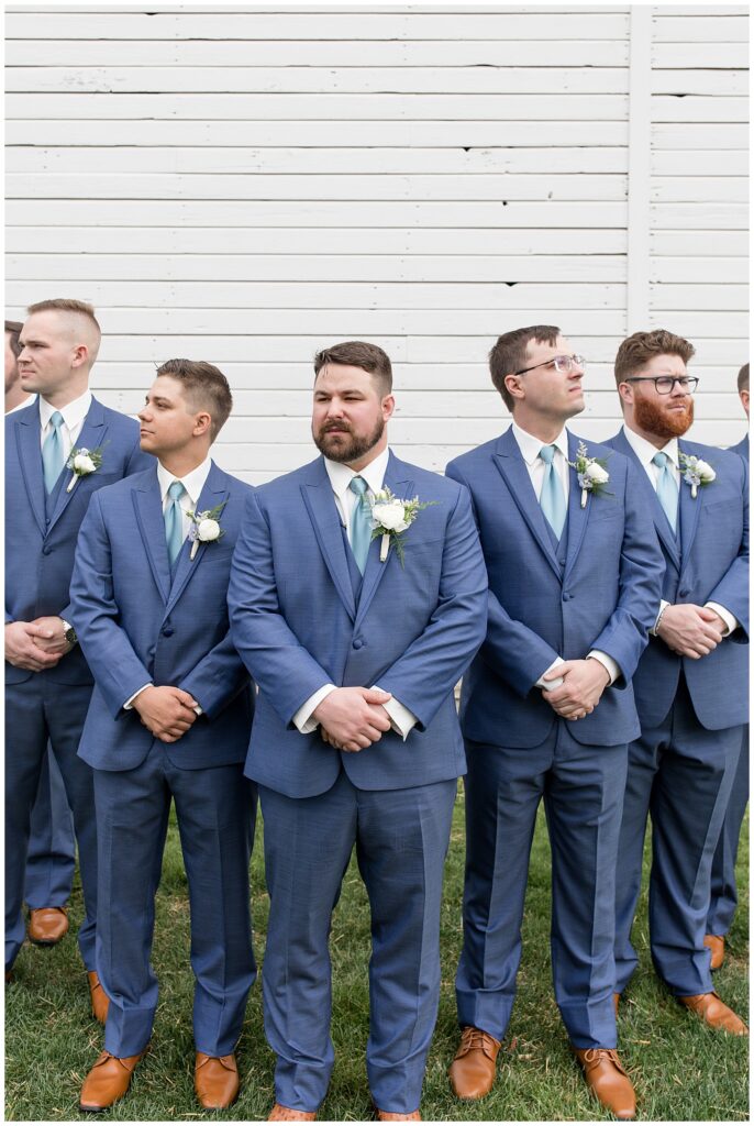 groom with his six groomsmen wearing blue suits by white barn in lancaster county