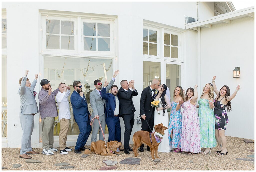 couple kissing as their bridal party cheers them on outside white building at lauxmont farms in york county pennsylvania