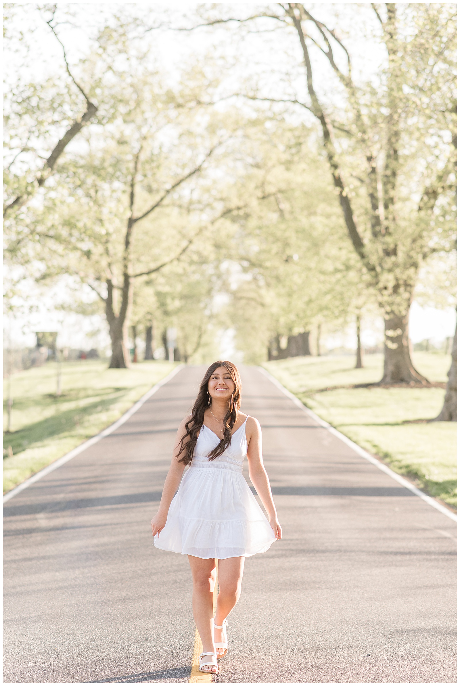 senior girl in white dress standing in middle of tree-lined road at masonic village in lancaster county