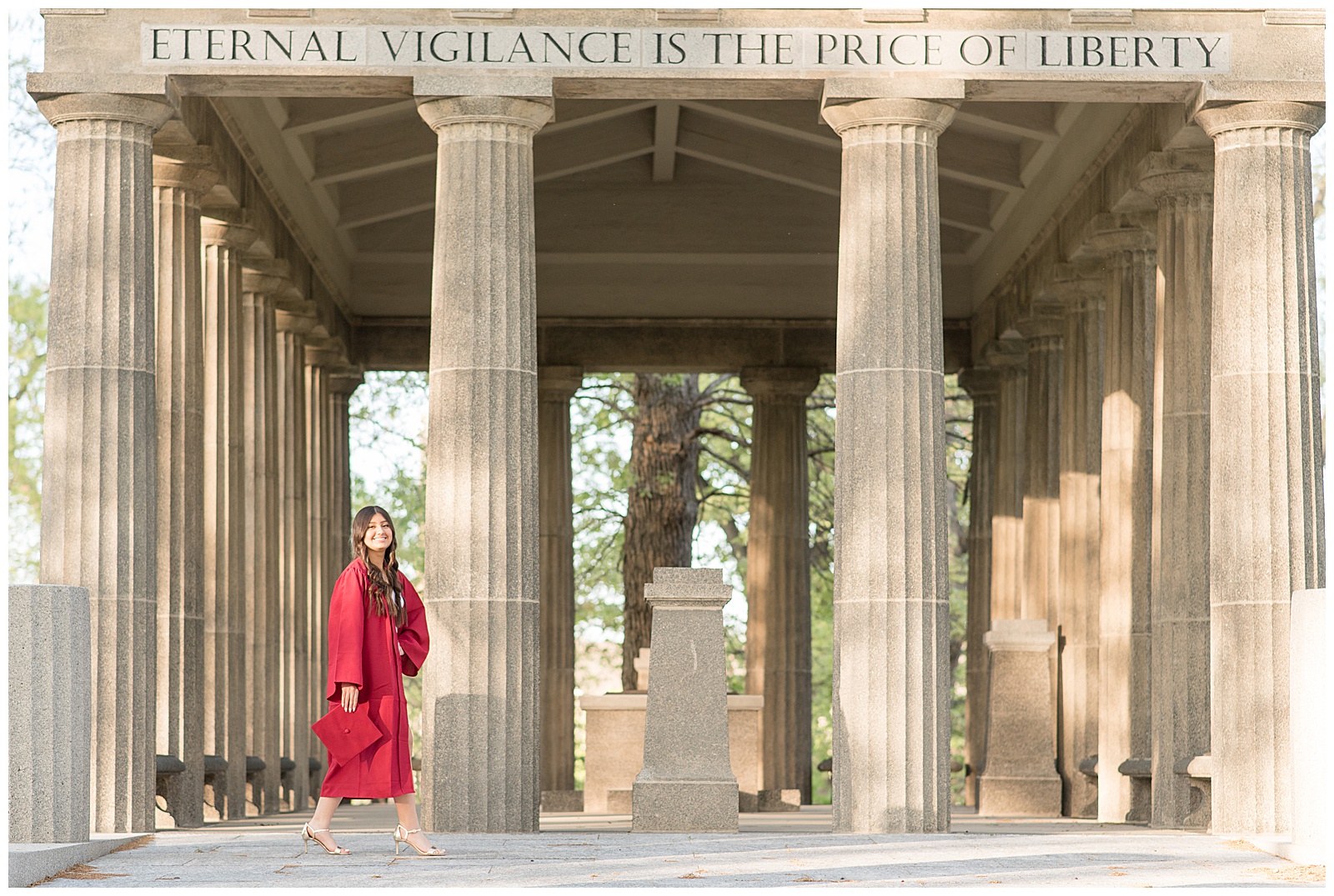 senior girl in red graduation gown standing by tall concrete columns at masonic village at sunset