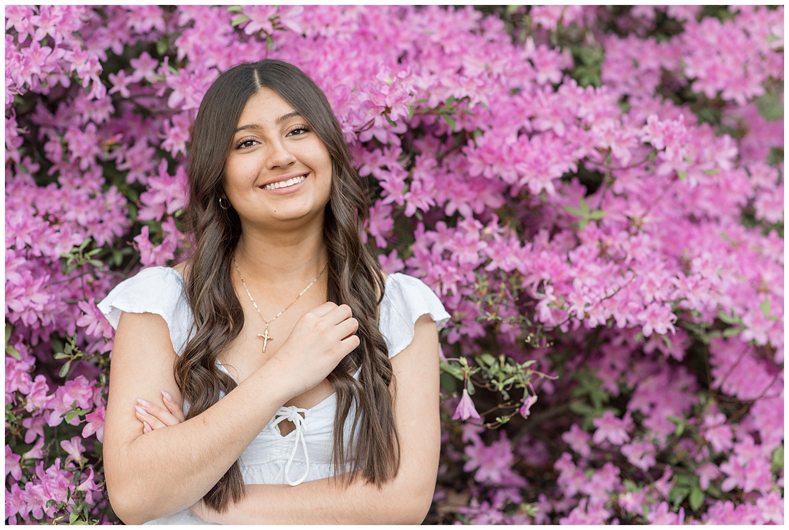 senior girl with arms folded standing by beautiful pink bush in lancaster county pennsylvania