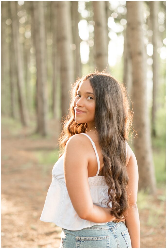 senior girl wearing white tank top and blue jeans looking back over left shoulder at overlook park
