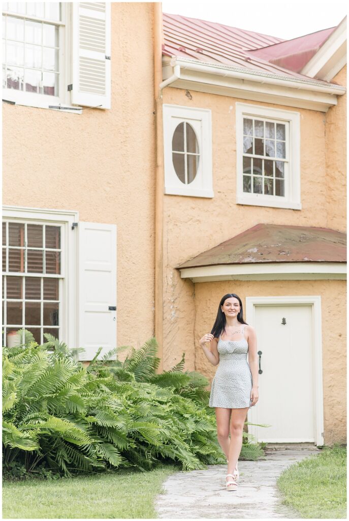 senior girl standing by peach and white home at hibernia park in chester county pa