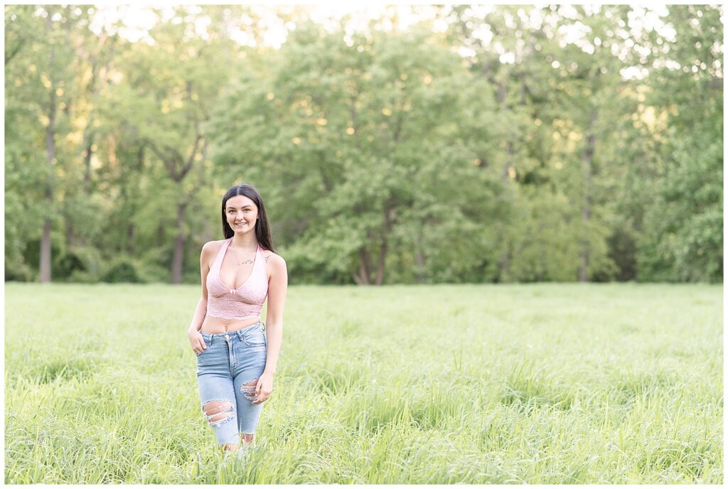 senior girl wearing tank top and blue jeans in grass field at hibernia park in coatesville pennsylvania