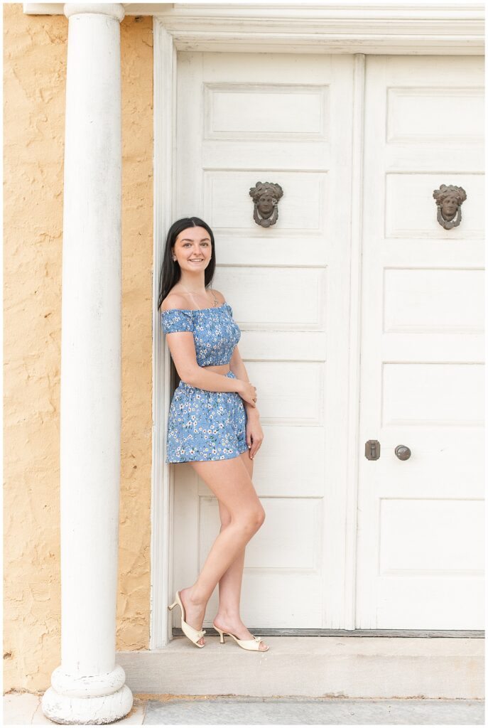 senior girl leaning against door frame of peach and white home at hibernia park