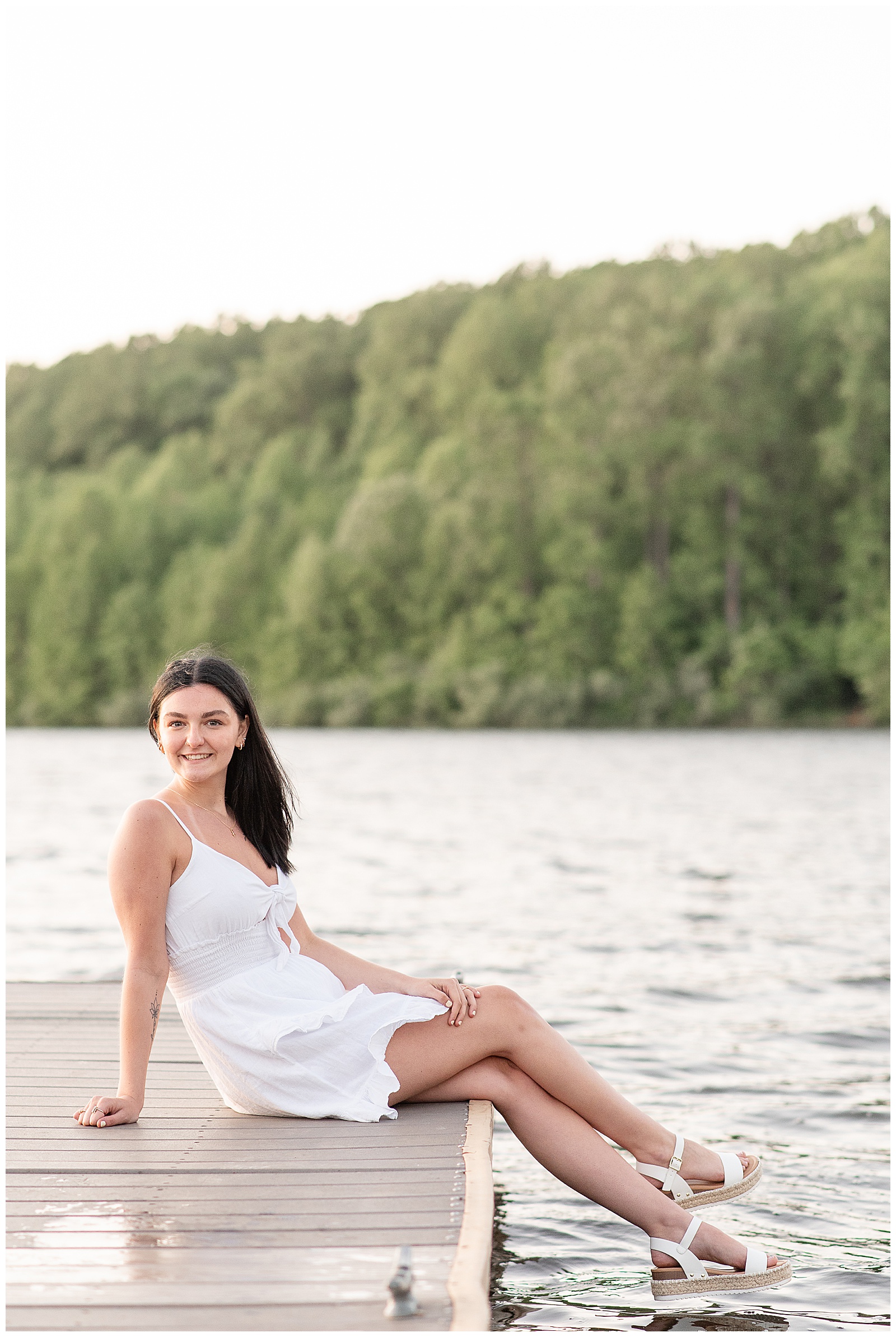senior girl in cute white dress sitting on dock by pond at hibernia park