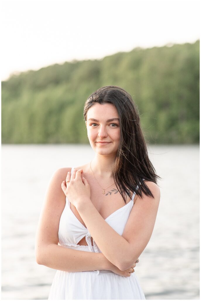 senior girl smiling at camera with left hand on right shoulder by pond at hibernia park
