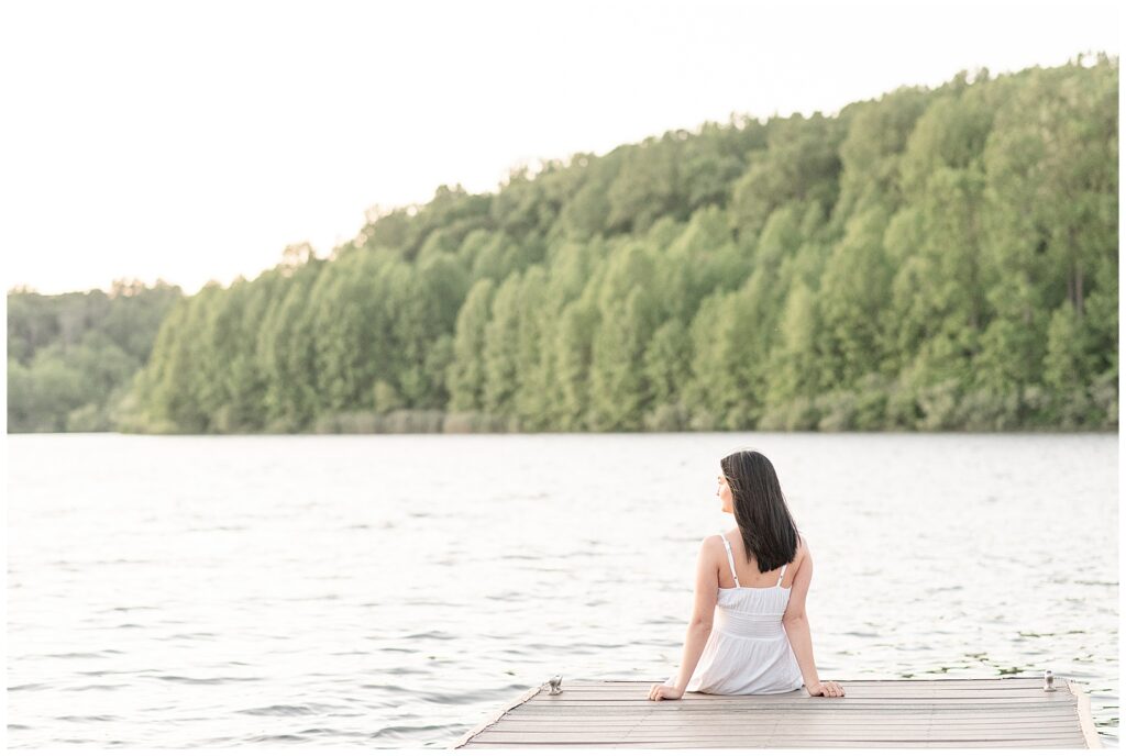 senior girl sitting on edge of dock with her back toward camera at this spring hibernia park senior session