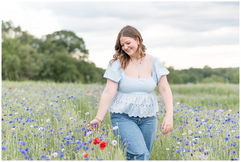 senior girl looking down and smiling at purple, red, and white flowers for this wildflower field senior session