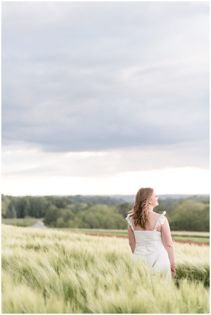 senior girl with her back to the camera wearing white dress and looking over her right shoulder for this wildflower field senior session