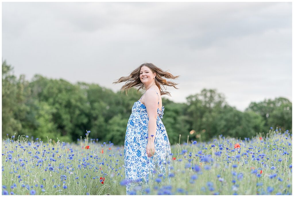 class of 2025 senior girl in blue and white dress spinning in wildflower field senior session in lancaster pennsylvania