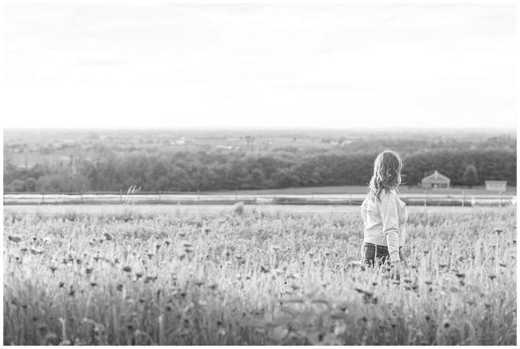 black and white photo of senior girl walking towards the right side of photo in wildflower field senior session in lancaster pa