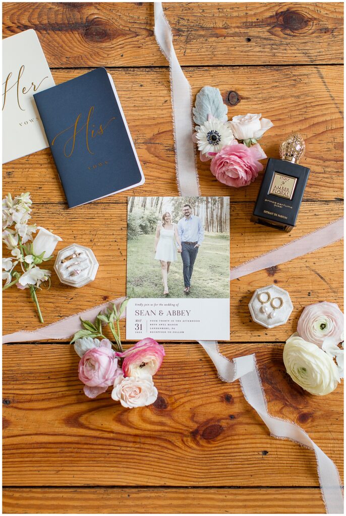 lovely wedding details including the wedding invitation, rings, and flowers on wooden table for this Bryn Awel Manor Summer Wedding