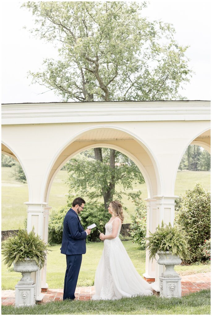 bride and groom read notes to one another by concrete archway at bryn awel manor on spring wedding day