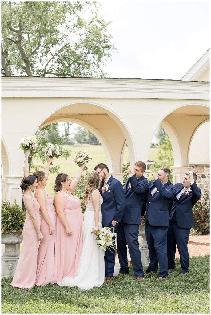 couple kissing with their bridal party around them by archway at this Bryn Awel Manor Summer Wedding