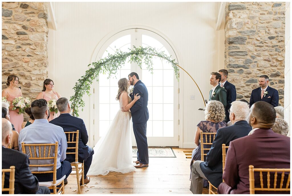 couple sharing their first kiss during indoor wedding ceremony at this Bryn Awel Manor Summer Wedding