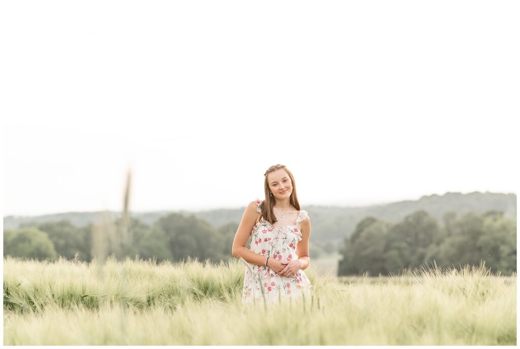 senior girl in floral dress standing in tall grasses at this Senior Wildflower Lookout Session with the HMP spokesmodel team