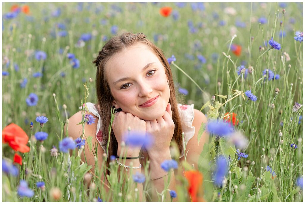 senior girl sitting surrounded by wildflower field with her chin resting on her fists for this Senior Wildflower Lookout Session