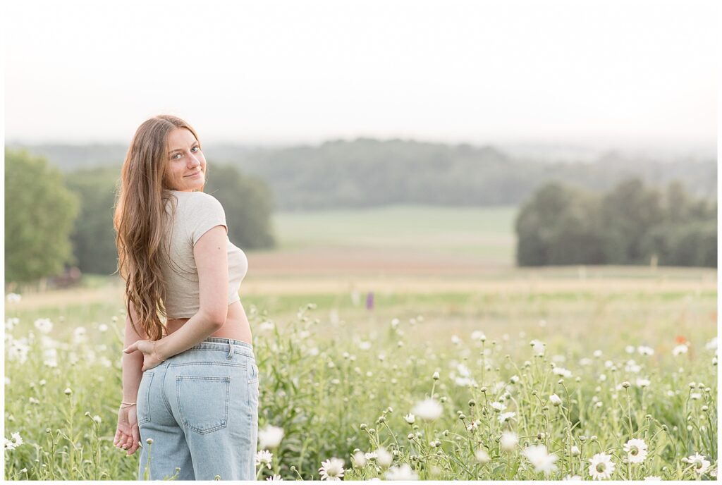 senior girl looking back over right shoulder in field of white wildflowers in lancaster county