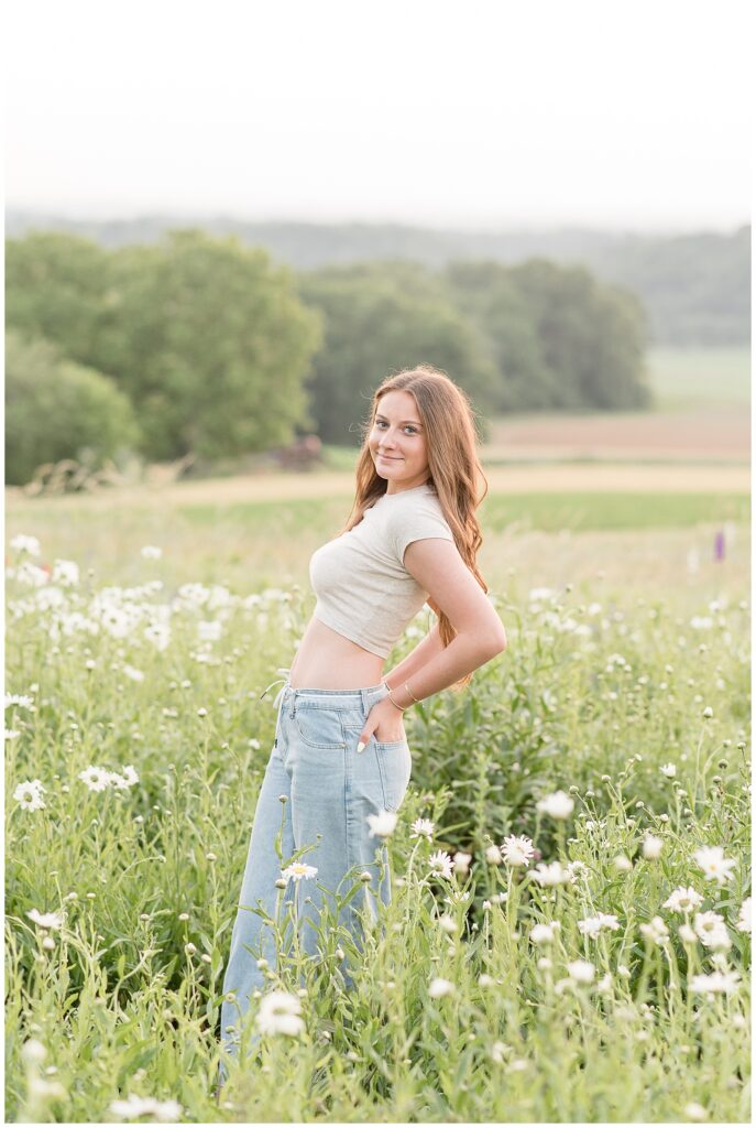 senior girl with hands in back pockets and leaning back for this Wildflower Field Summer Senior Session in lancaster pa
