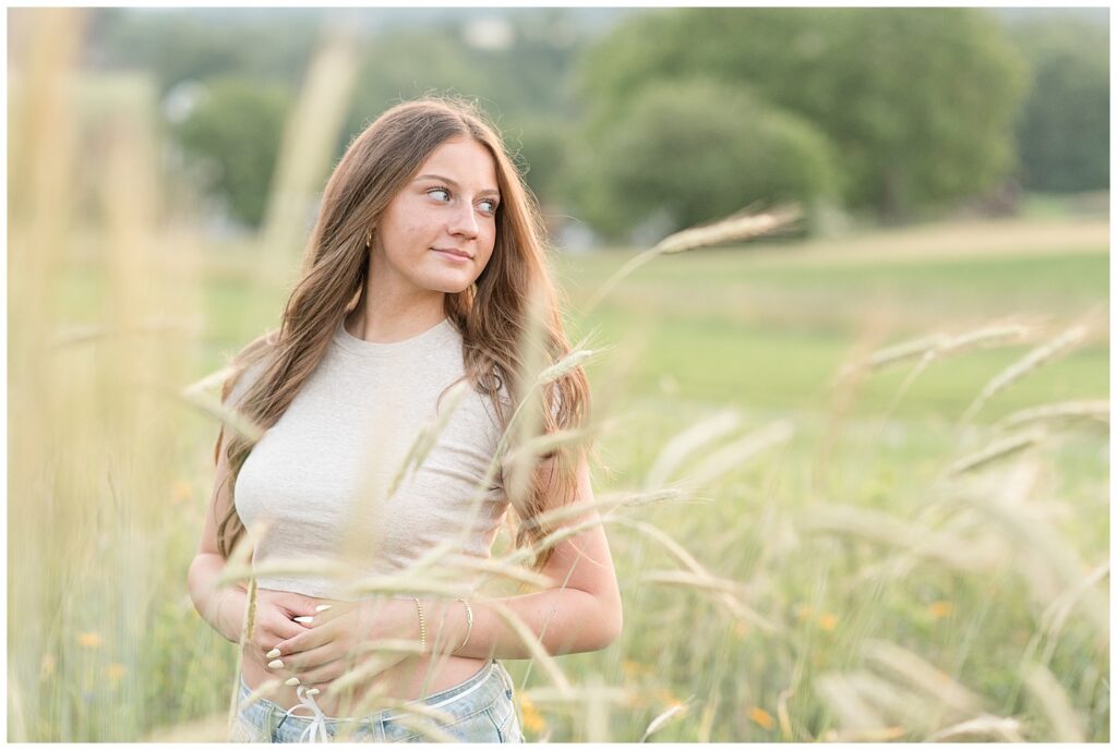 senior girl standing in wheat field and looking left at sunset for this Wildflower Field Summer Senior Session