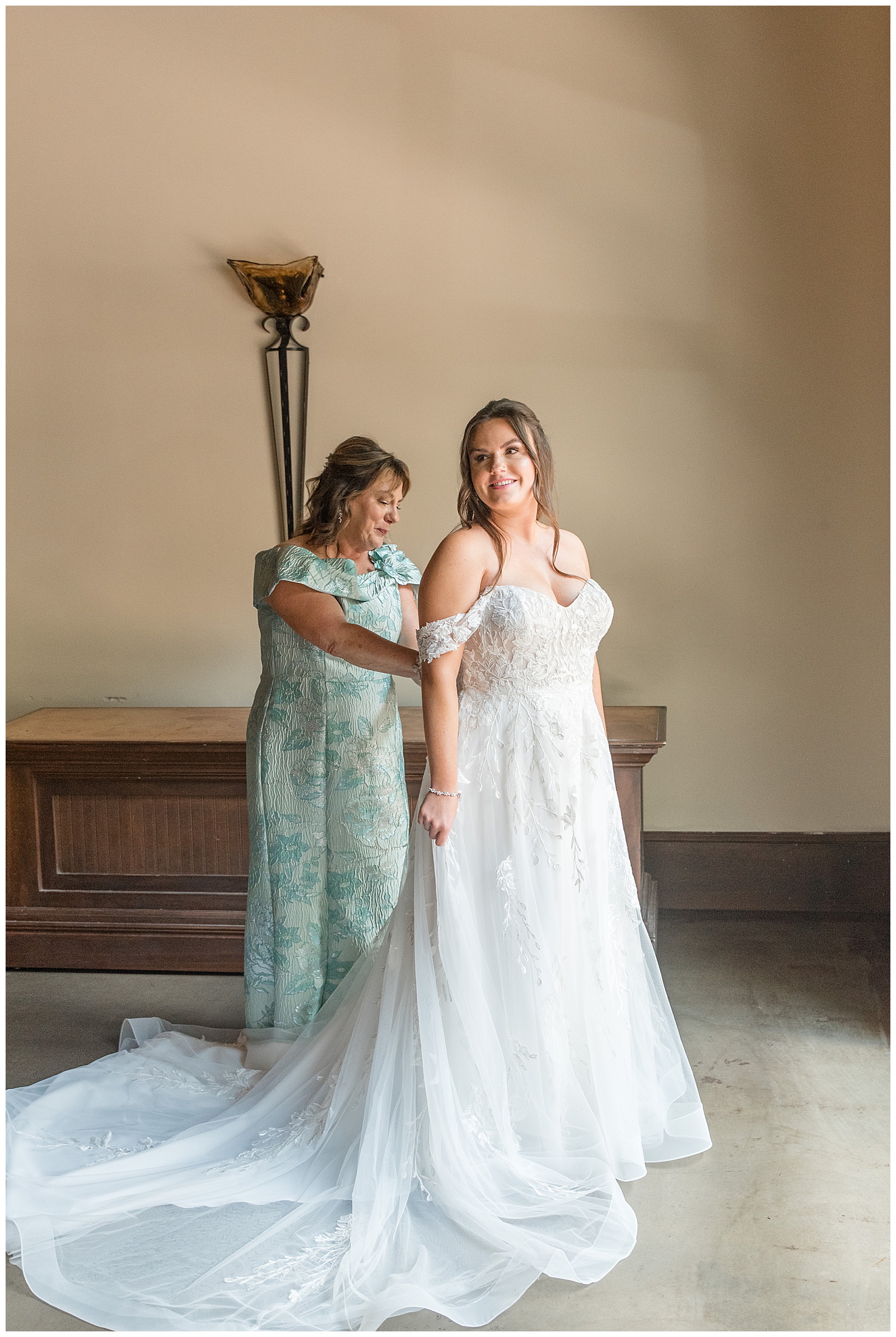 bride's mom in light blue dress zipping up bride's white gown at this Inn at Leola Village Wedding